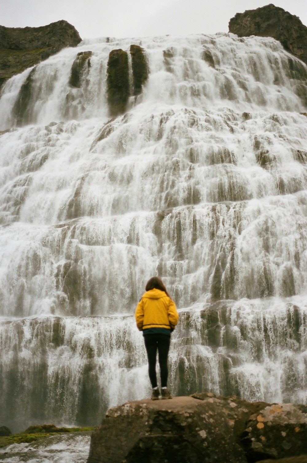 man in yellow hoodie standing in front of waterfalls