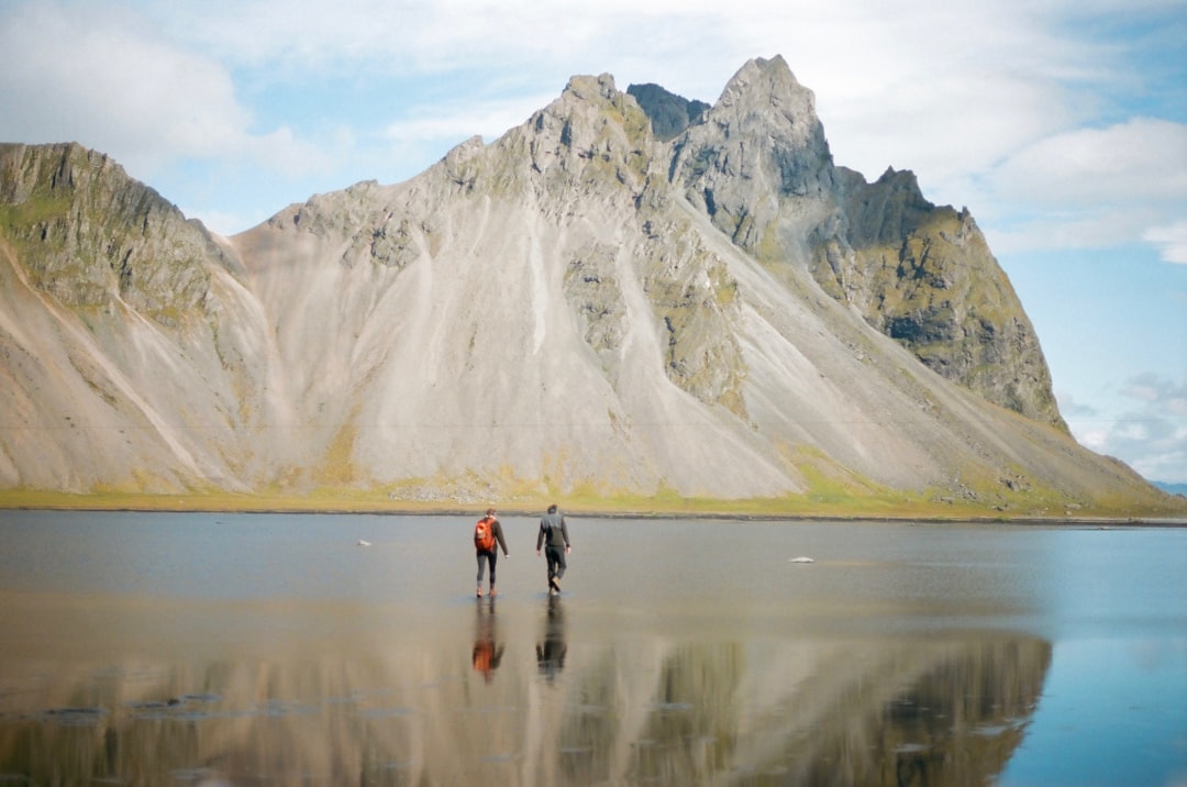 2 person walking on the beach near the snow covered mountain during daytime