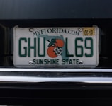A Florida license plate with the numbers and letters 'GHUL69'. It features the outline of the state and an orange graphic with blossoms. The text 'SUNSHINE STATE' is displayed at the bottom with the website 'MYFLORIDA.COM' at the top. There is a yellow sticker in the upper right corner indicating an expiration date of 06-19.