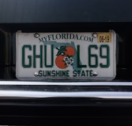 A Florida license plate with the numbers and letters 'GHUL69'. It features the outline of the state and an orange graphic with blossoms. The text 'SUNSHINE STATE' is displayed at the bottom with the website 'MYFLORIDA.COM' at the top. There is a yellow sticker in the upper right corner indicating an expiration date of 06-19.