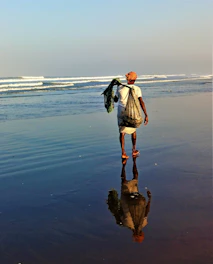 An elderly man standing barefoot on a rocky shore, gazing at the horizon under a soft sunset.