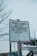 A weathered sign stands prominently, warning visitors that parklands are not to be treated as litterboxes for the sake of children. The bottom of the sign reminds readers to clean up after their pets. It is mounted on a wooden post and set against a background of bare trees and a snowy landscape, possibly in an urban setting.