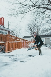 A person shoveling snow from a walkway with a bright winter sky.