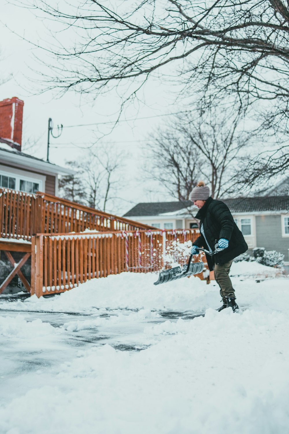 man in black jacket and black pants walking on snow covered ground near brown wooden fence