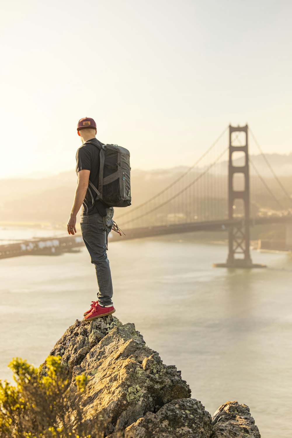 man in black jacket and blue denim jeans standing on rock near bridge during daytime