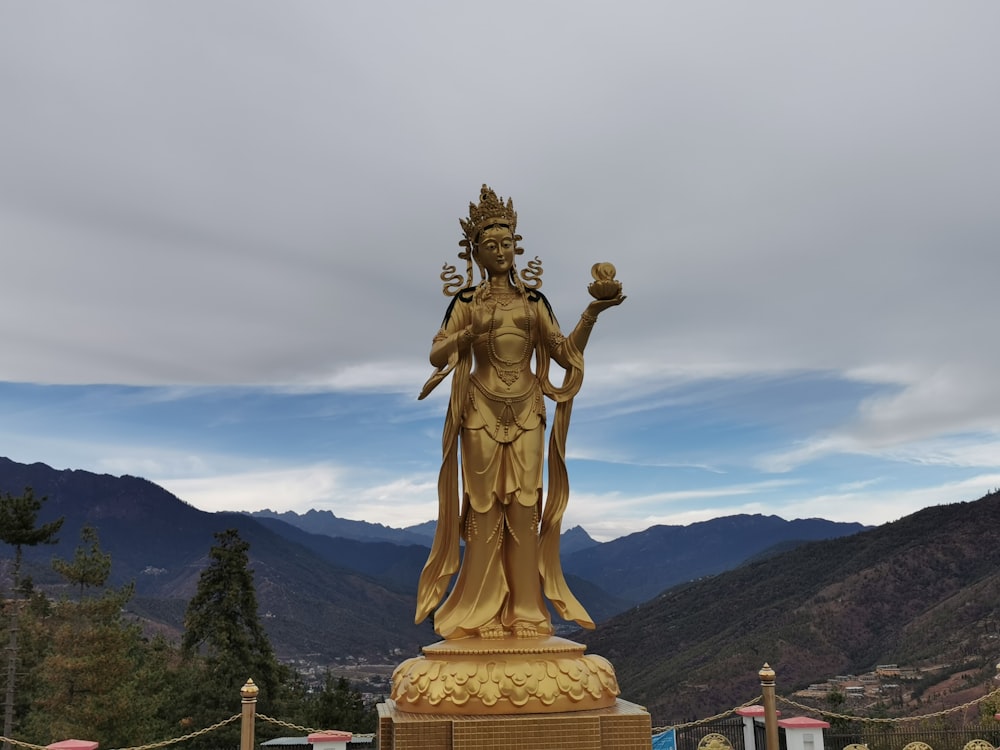 gold statue of woman with a distance at mountain under white clouds during daytime