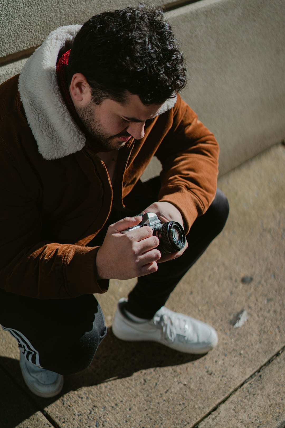 man in brown jacket and black pants holding black and silver dslr camera
