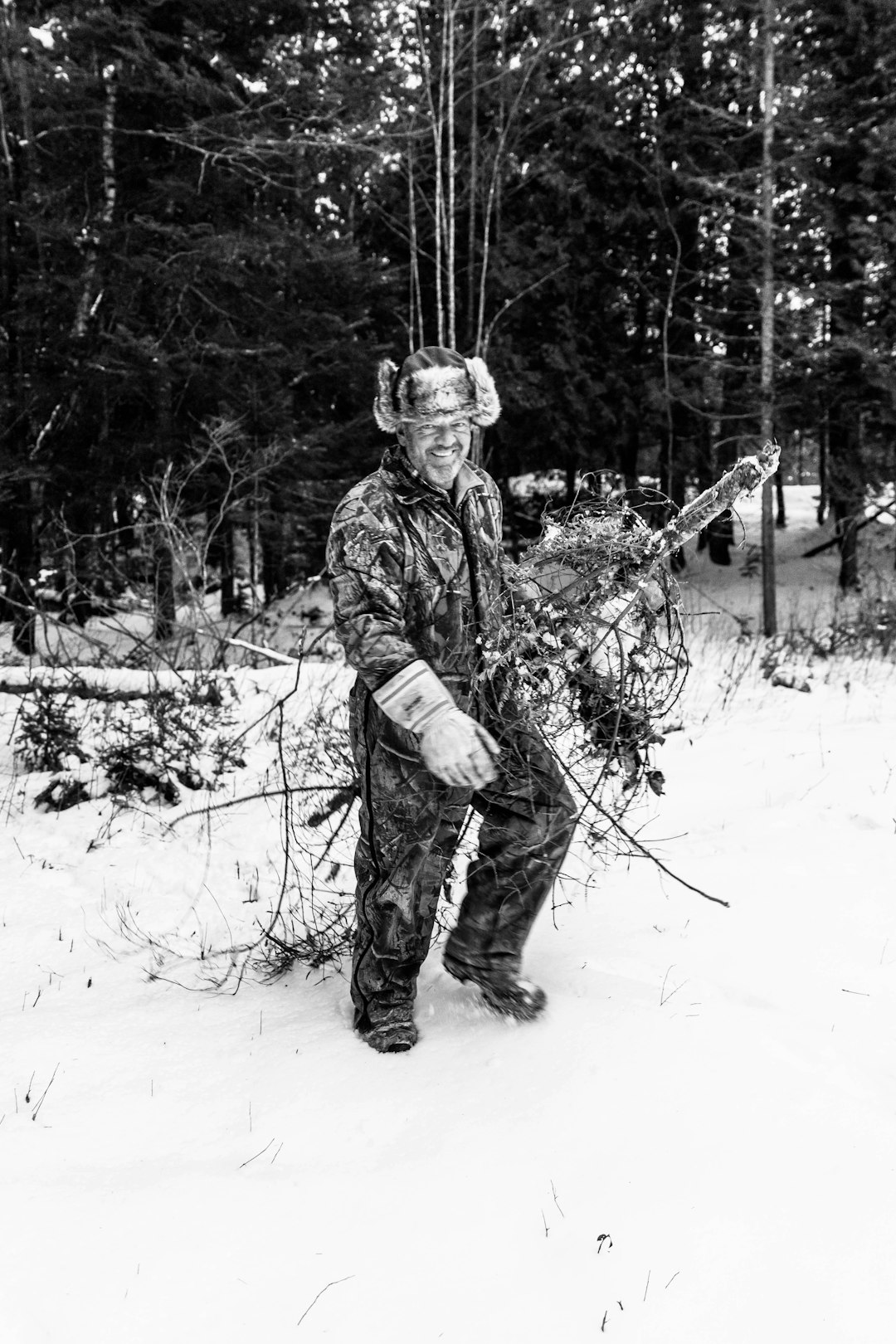 grayscale photo of man in camouflage jacket standing on snow covered ground