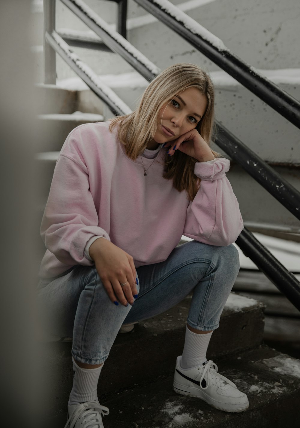 woman in pink sweater and blue denim jeans sitting on black metal railings