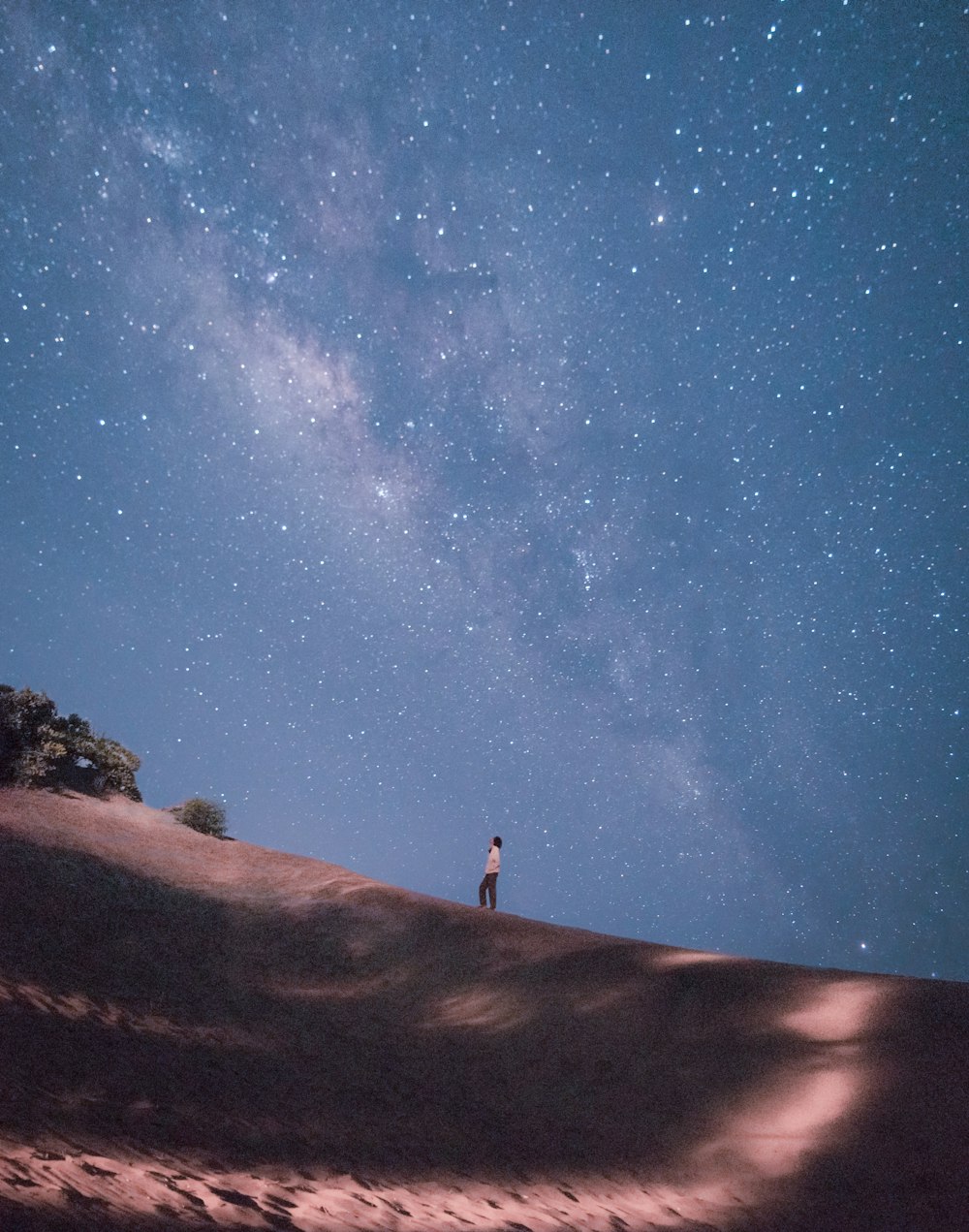 Persona in piedi su sabbia marrone sotto il cielo blu durante il giorno