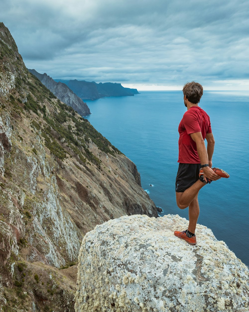 man in blue shirt and black shorts standing on rock formation near body of water during