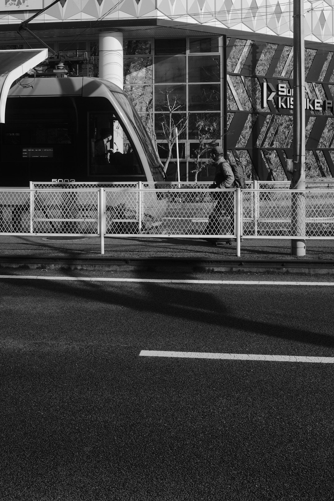 grayscale photo of woman in black jacket standing beside fence