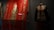 A richly embroidered red textile features intricate designs and figures, including a standing figure in traditional attire. To the right, a mannequin displays a dark, intricately patterned jacket with floral motifs and a similar traditional style.