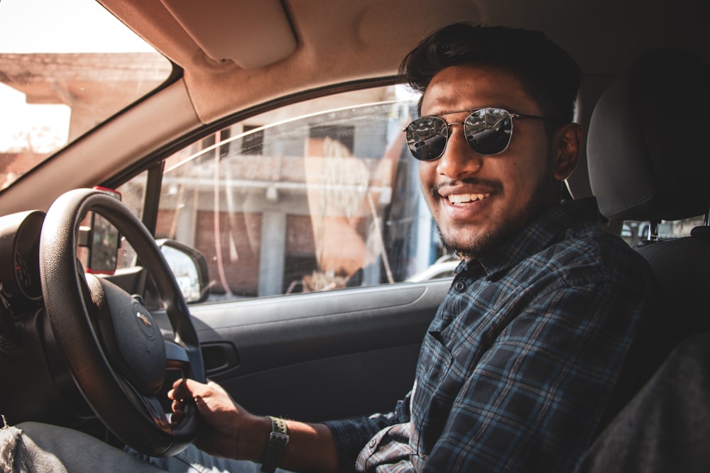 man in black and white plaid dress shirt wearing black sunglasses driving car