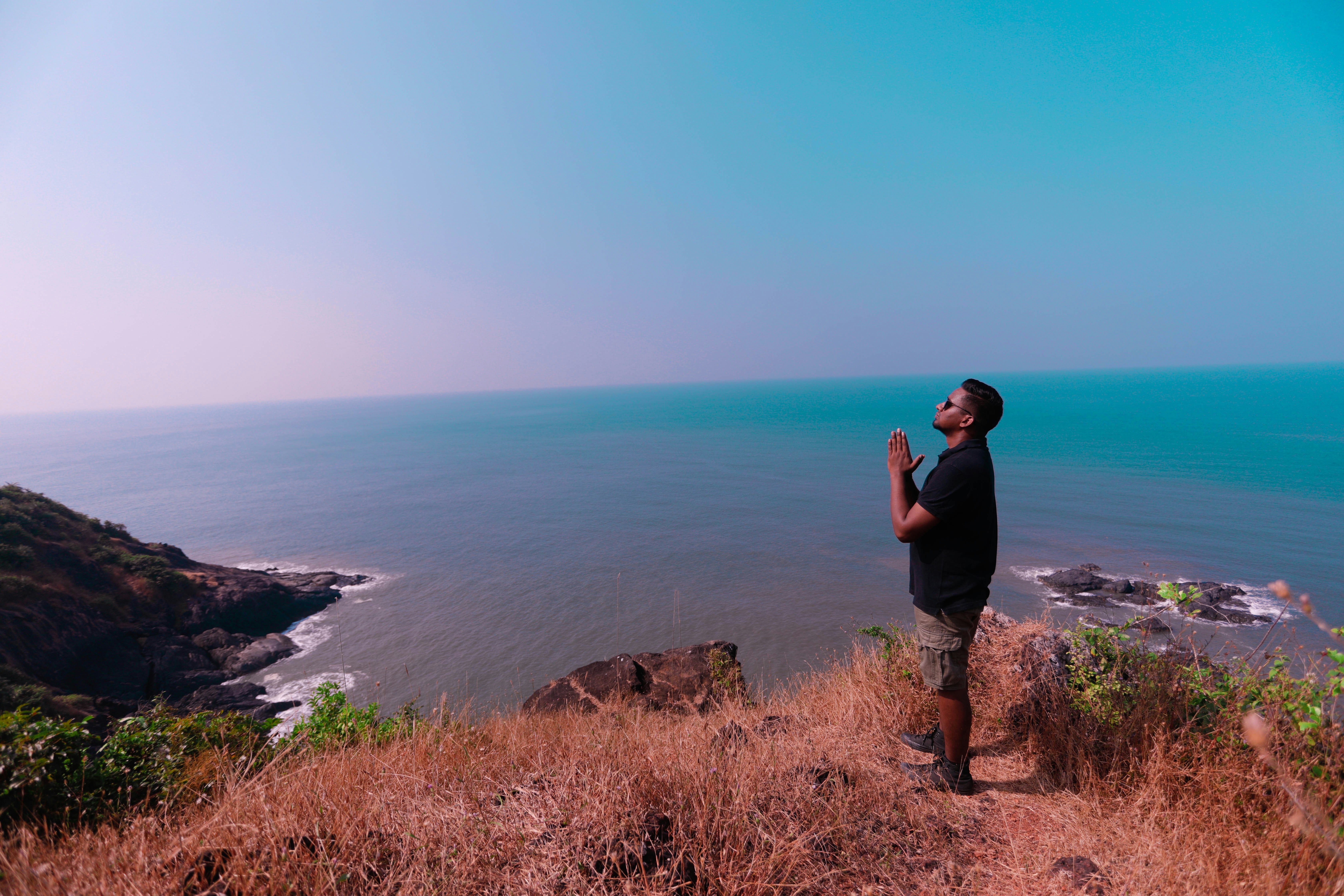 man in black t-shirt standing on brown rock formation near blue sea during daytime
