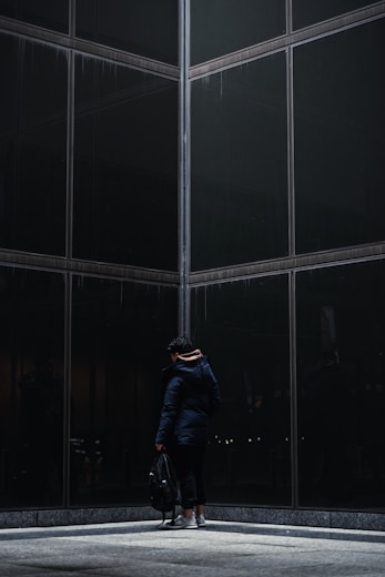 man in blue jacket and black pants standing in front of black building
