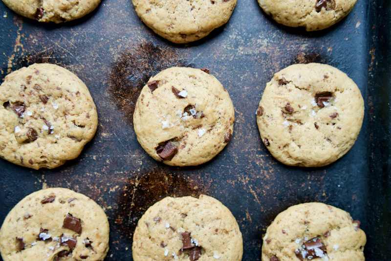 Golden cookies with big chocolate chunks on a dark baking tray
