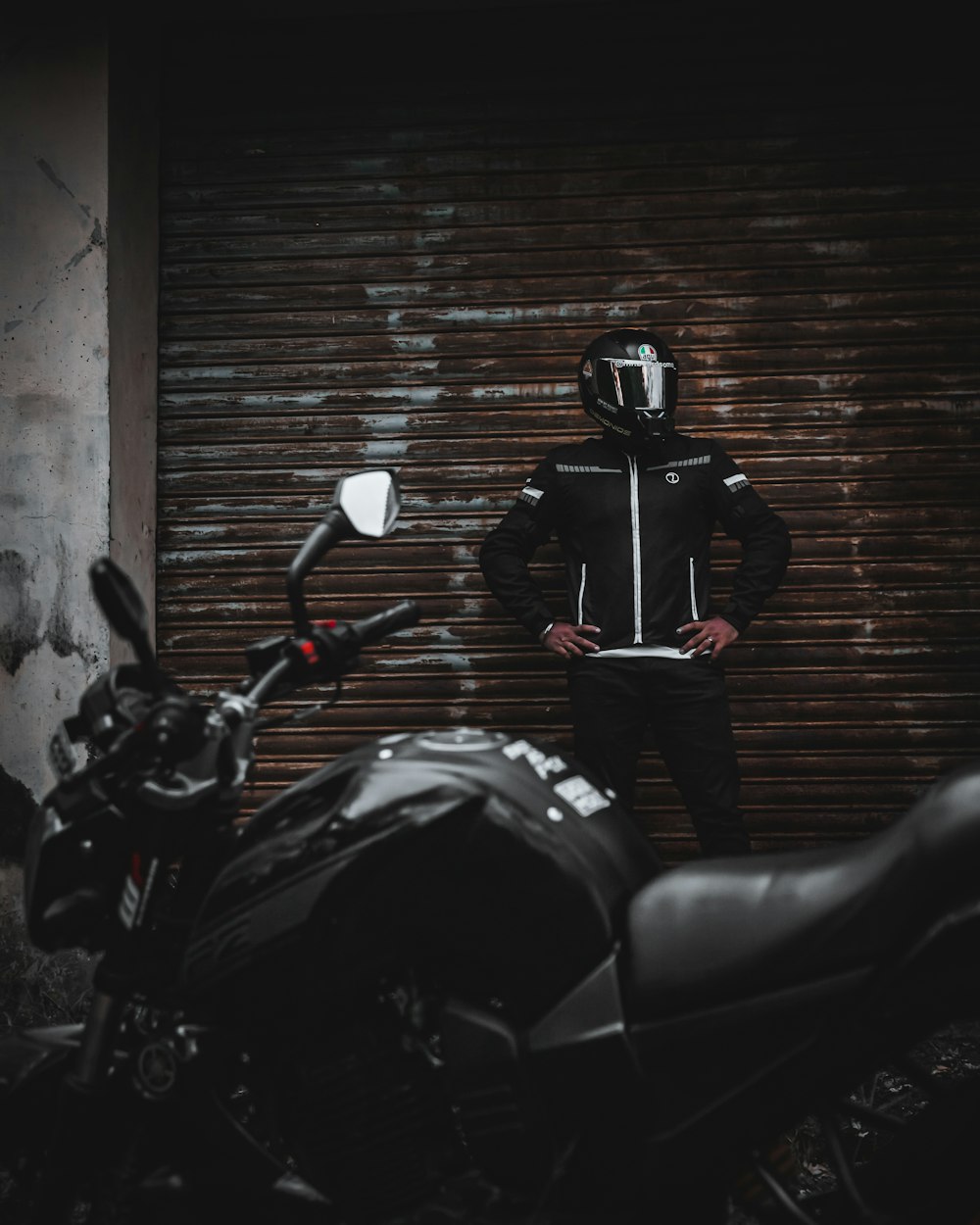 man in black jacket and black pants standing beside black sports bike