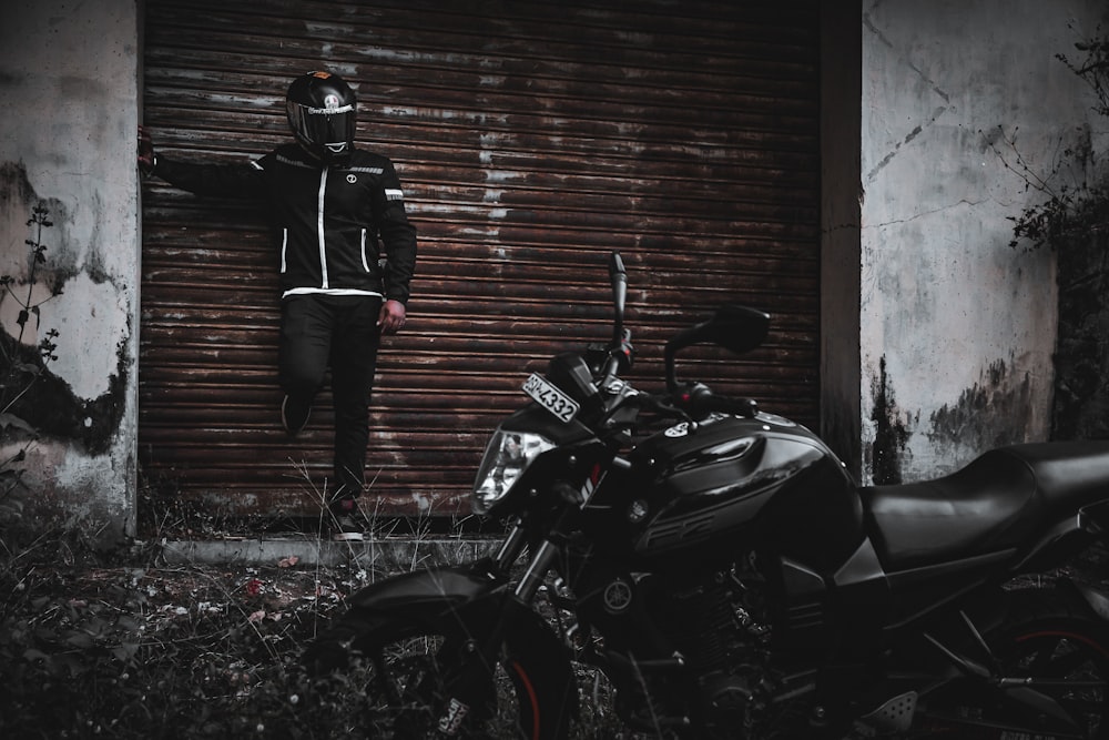 man in black jacket and black pants standing beside black sports bike