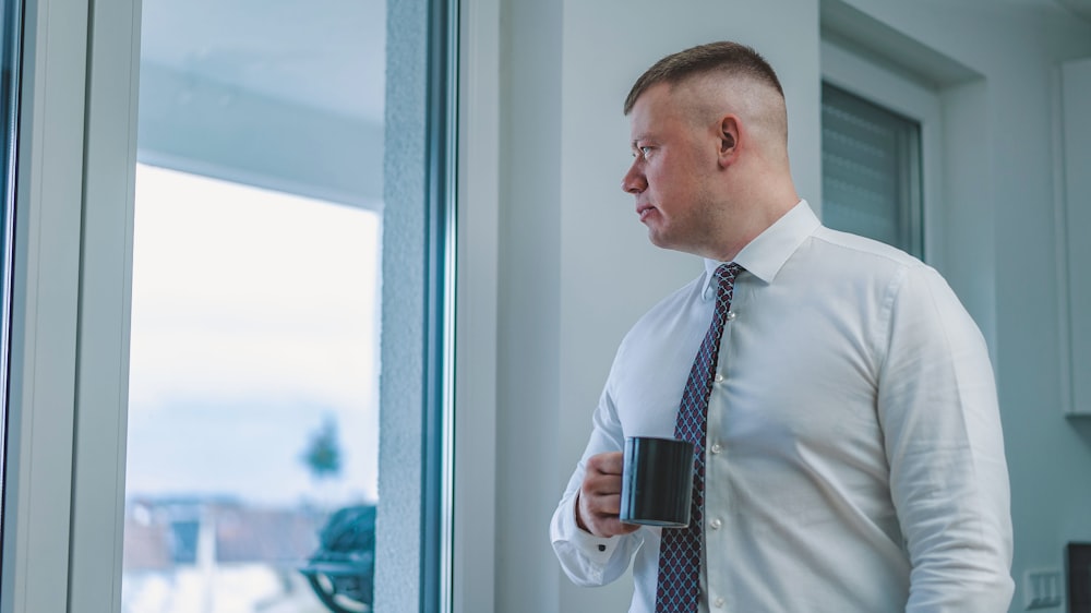 man in white dress shirt standing beside window during daytime