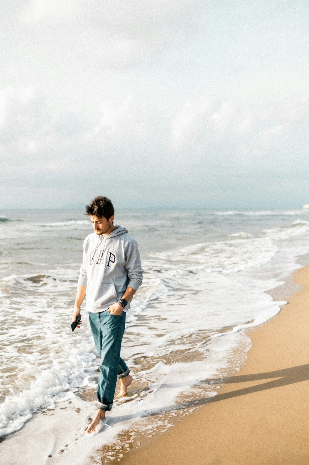 회색 긴팔 셔츠와 녹색 반바지를 입은 남자가 낮 동안 해변에 서 있다