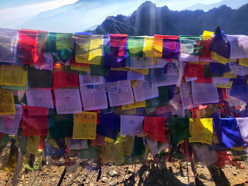 Pilgrims walking along a winding mountain trail surrounded by vibrant prayer flags fluttering in the breeze.
