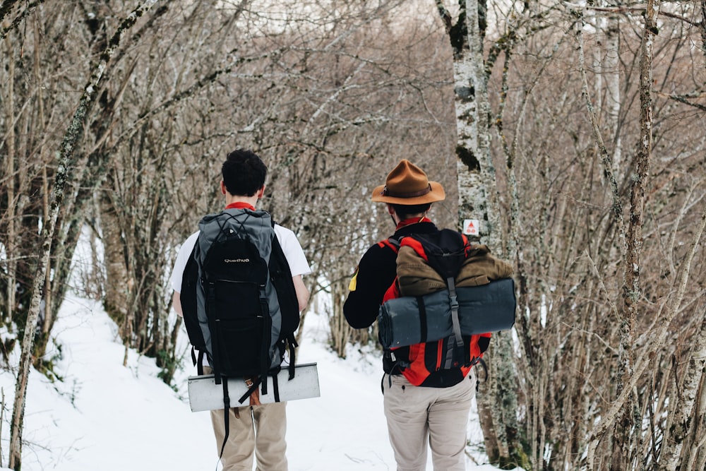 man in black jacket and white pants with black backpack walking on snow covered ground during