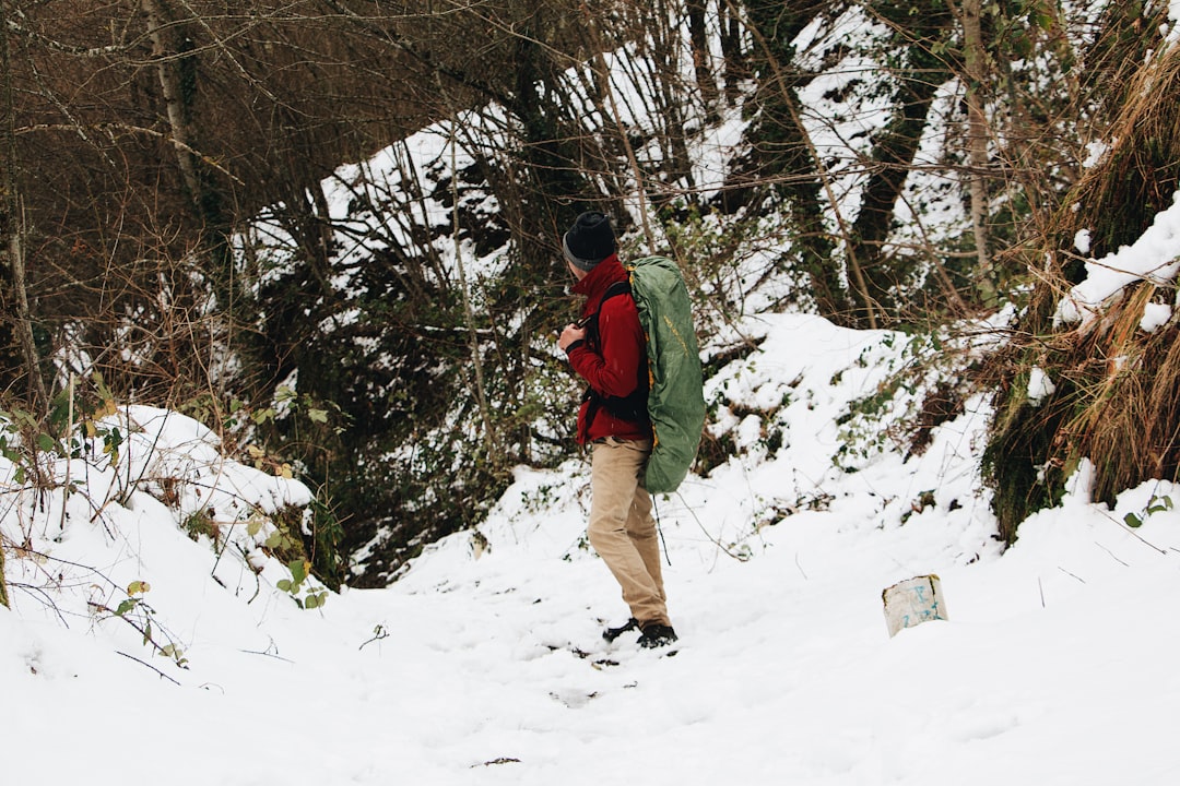 man in green jacket and brown pants walking on snow covered ground during daytime