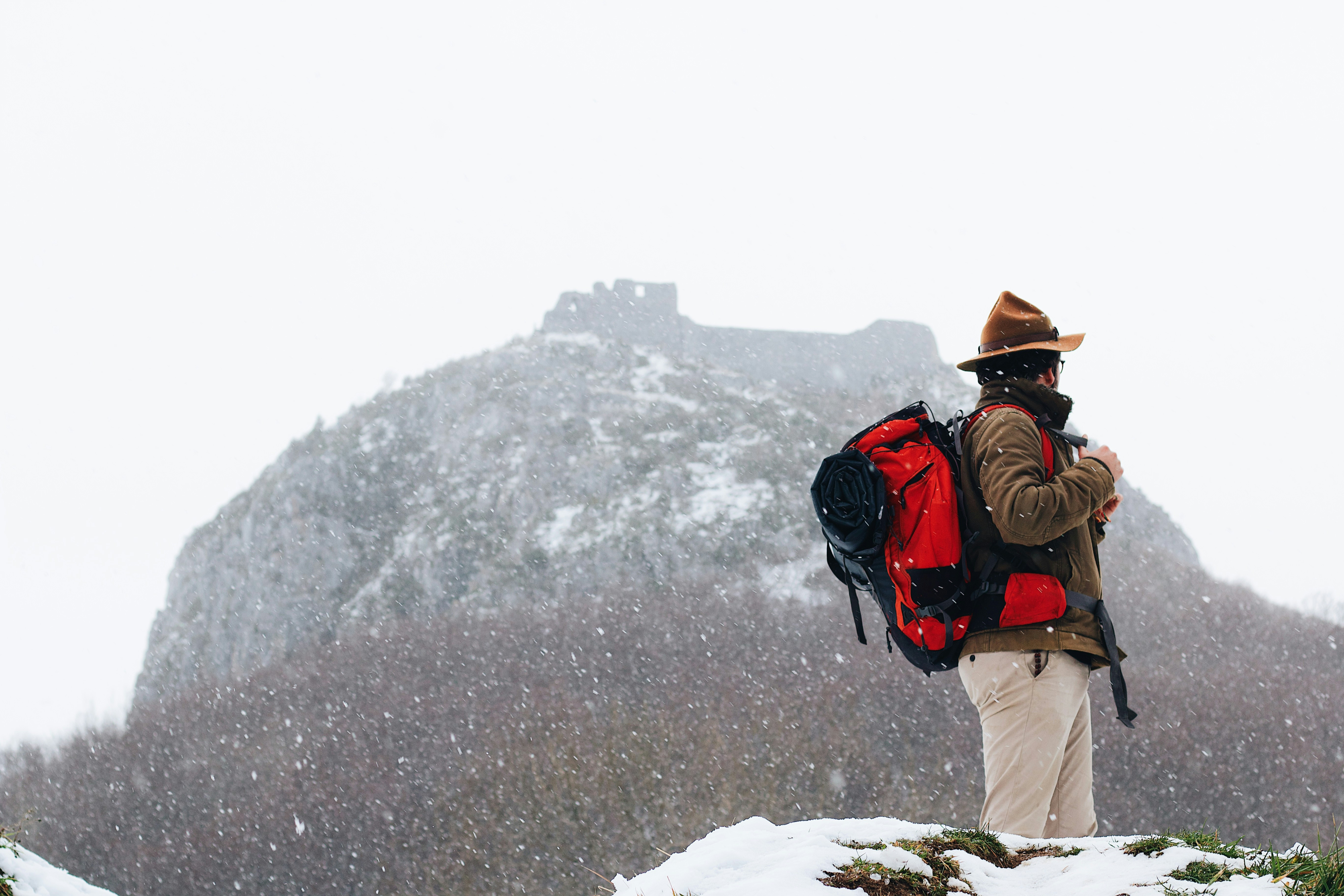 How to Travel During Peak Season Without the Stress or High Prices – man in brown jacket and beige pants carrying black backpack standing on rocky hill during daytime