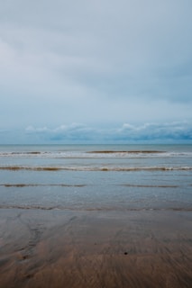 A calm beach with gentle waves under a cloudy sky.