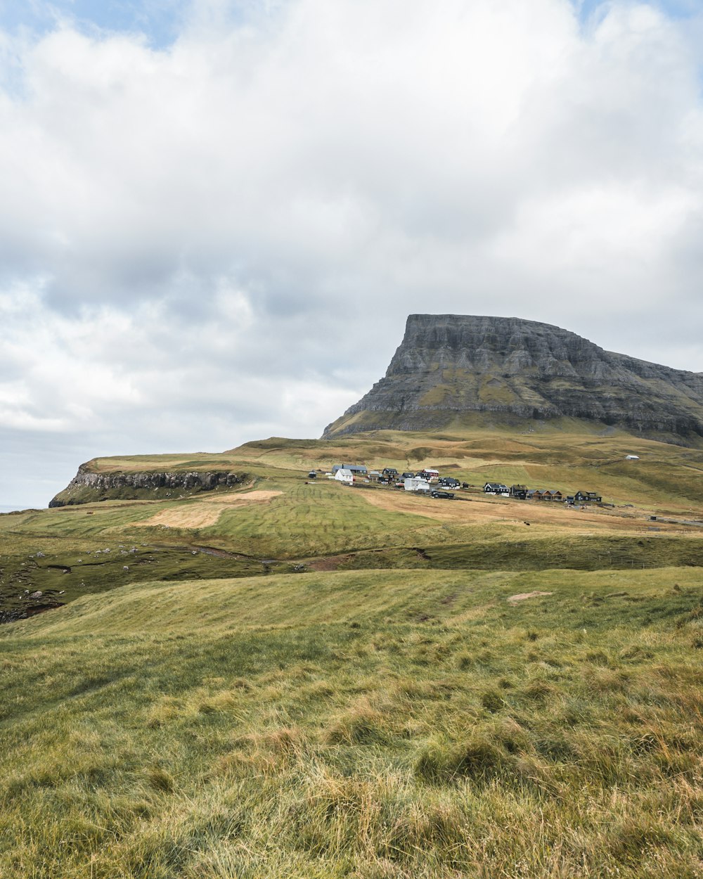 green grass field near mountain under white clouds during daytime