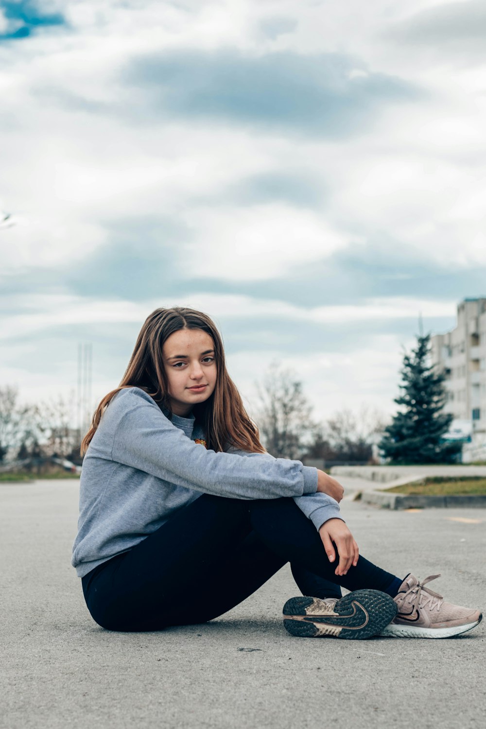 woman in gray sweater and black pants sitting on gray concrete pavement during daytime