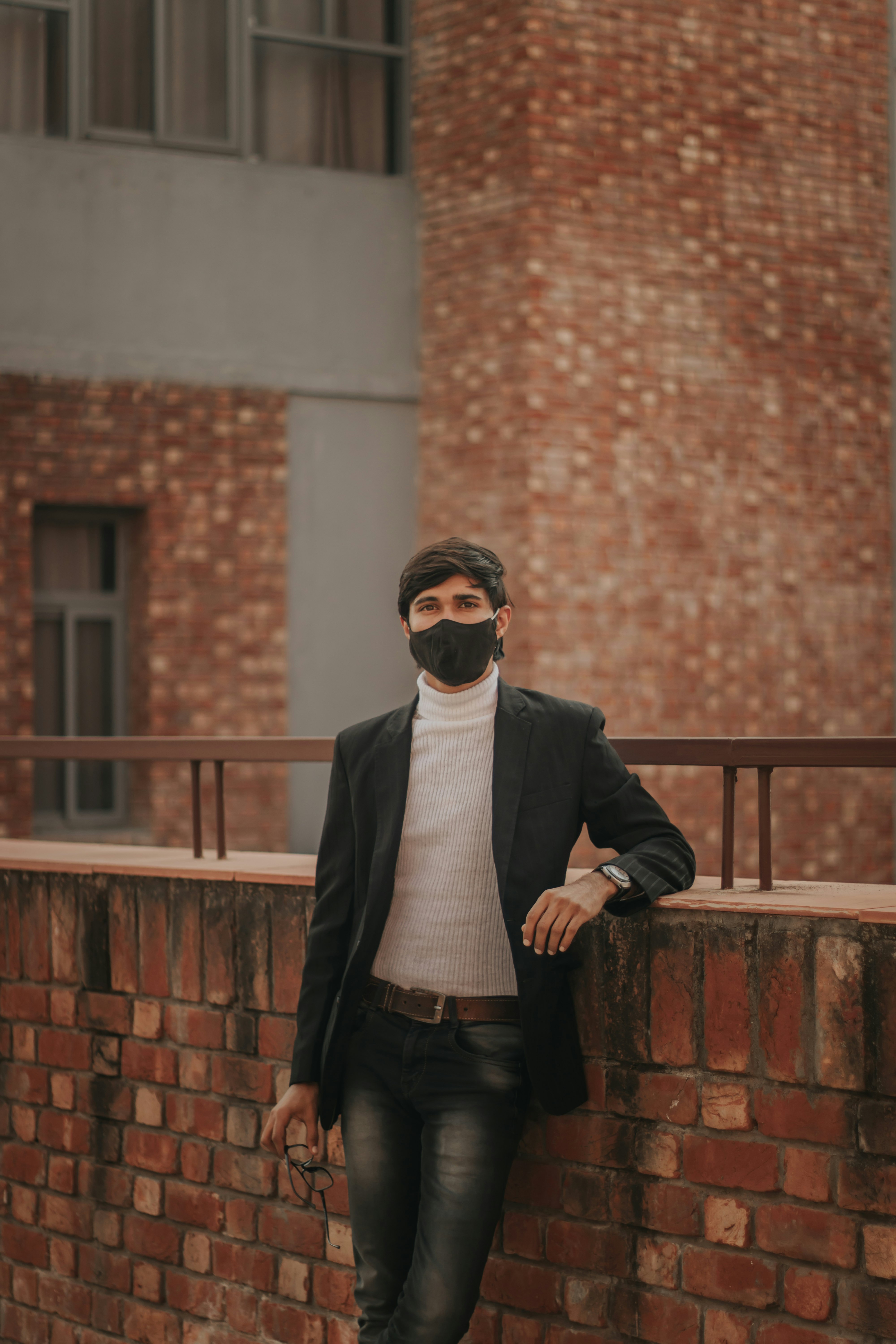 man in black suit jacket and black pants wearing black sunglasses standing near brown brick wall