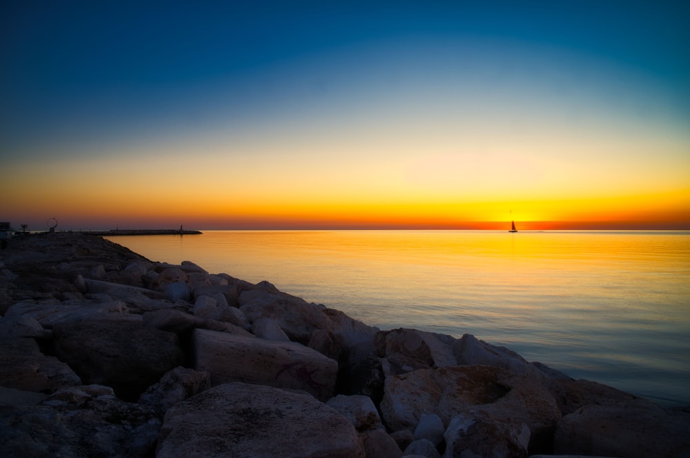 Rocas marrones cerca del cuerpo de agua durante la puesta del sol