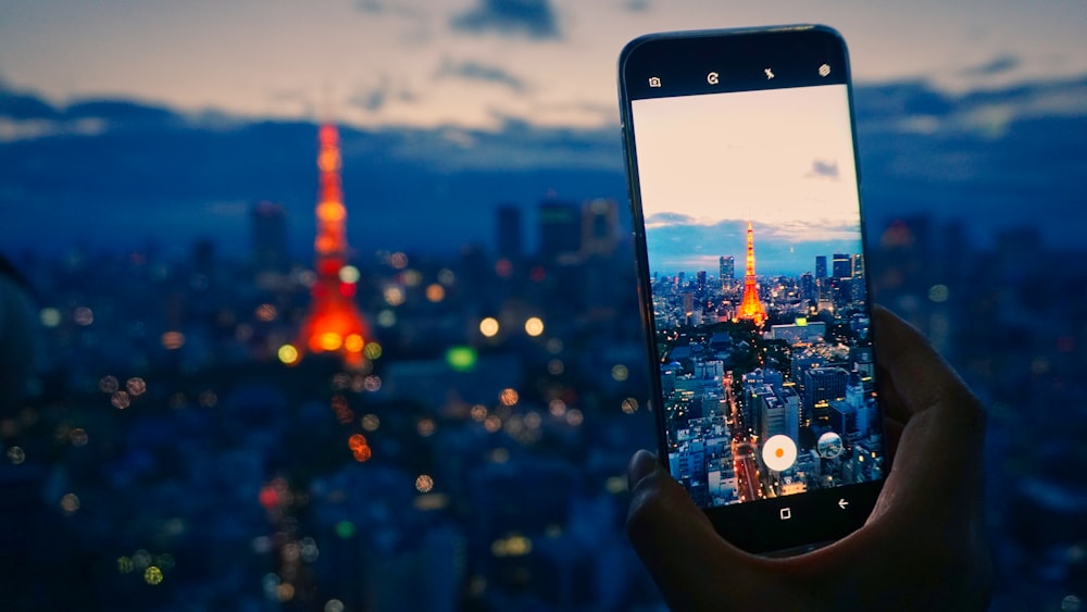 person holding smartphone taking photo of city buildings during night time