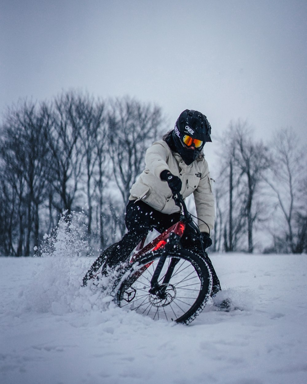 homem em jaqueta branca andando em mountain bike preto no chão coberto de neve durante o dia