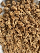 A collection of irregularly shaped brown solid chunks, likely some form of sweet or food item, with a grainy texture. The chunks are piled on a light-colored surface.