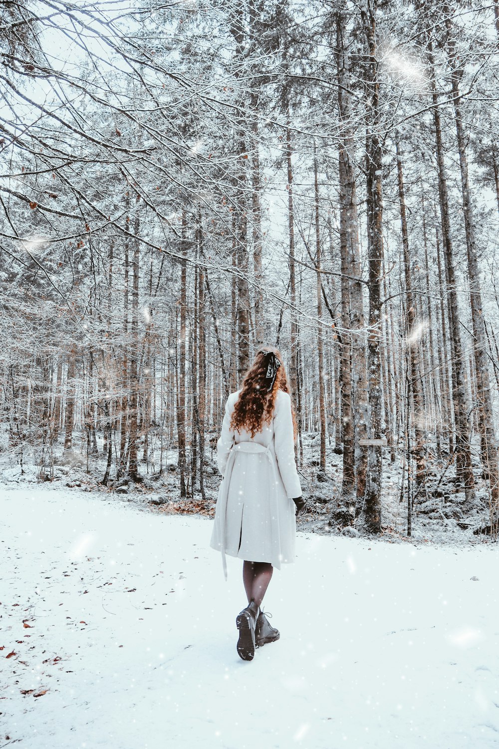 woman in white dress standing on snow covered ground surrounded by bare trees during daytime