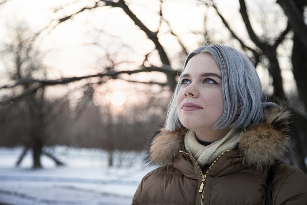 woman in brown fur lined jacket standing near bare trees during daytime