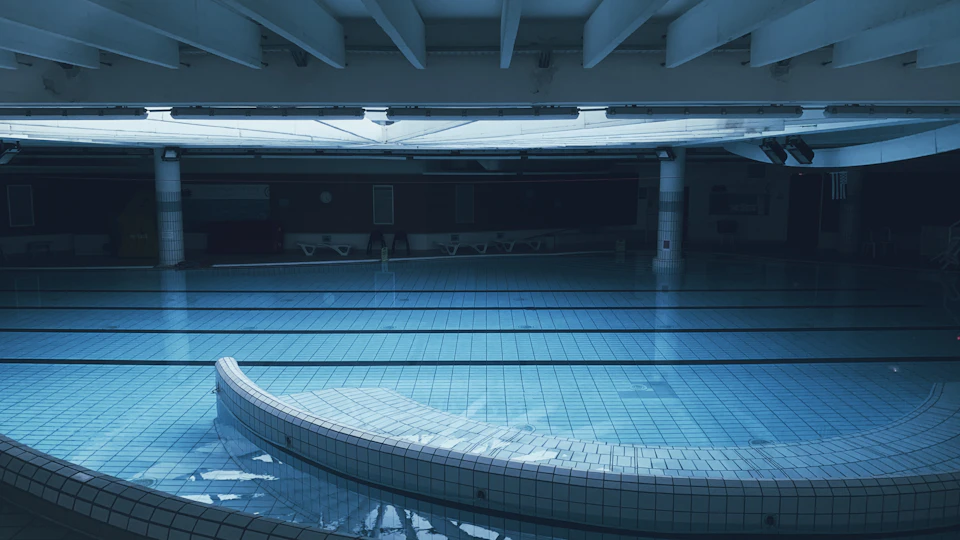Large empty swimming pool with curved white edge and blue interior surrounded by white pillars