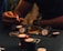 A hand holding several poker chips, with a glass of whiskey and a stack of poker chips on a table. The setting appears to be a dimly lit environment, suggesting an intimate or focused atmosphere.
