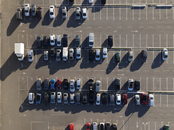 Aerial video still showing vehicles entering and leaving a busy parking lot with occupied and empty spaces.