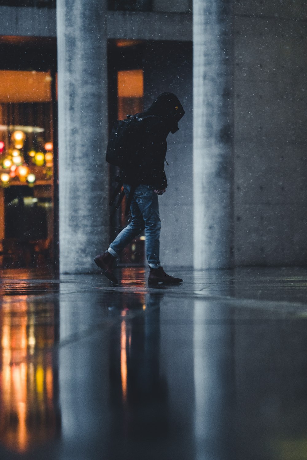 man in black jacket and blue denim jeans standing on gray concrete floor