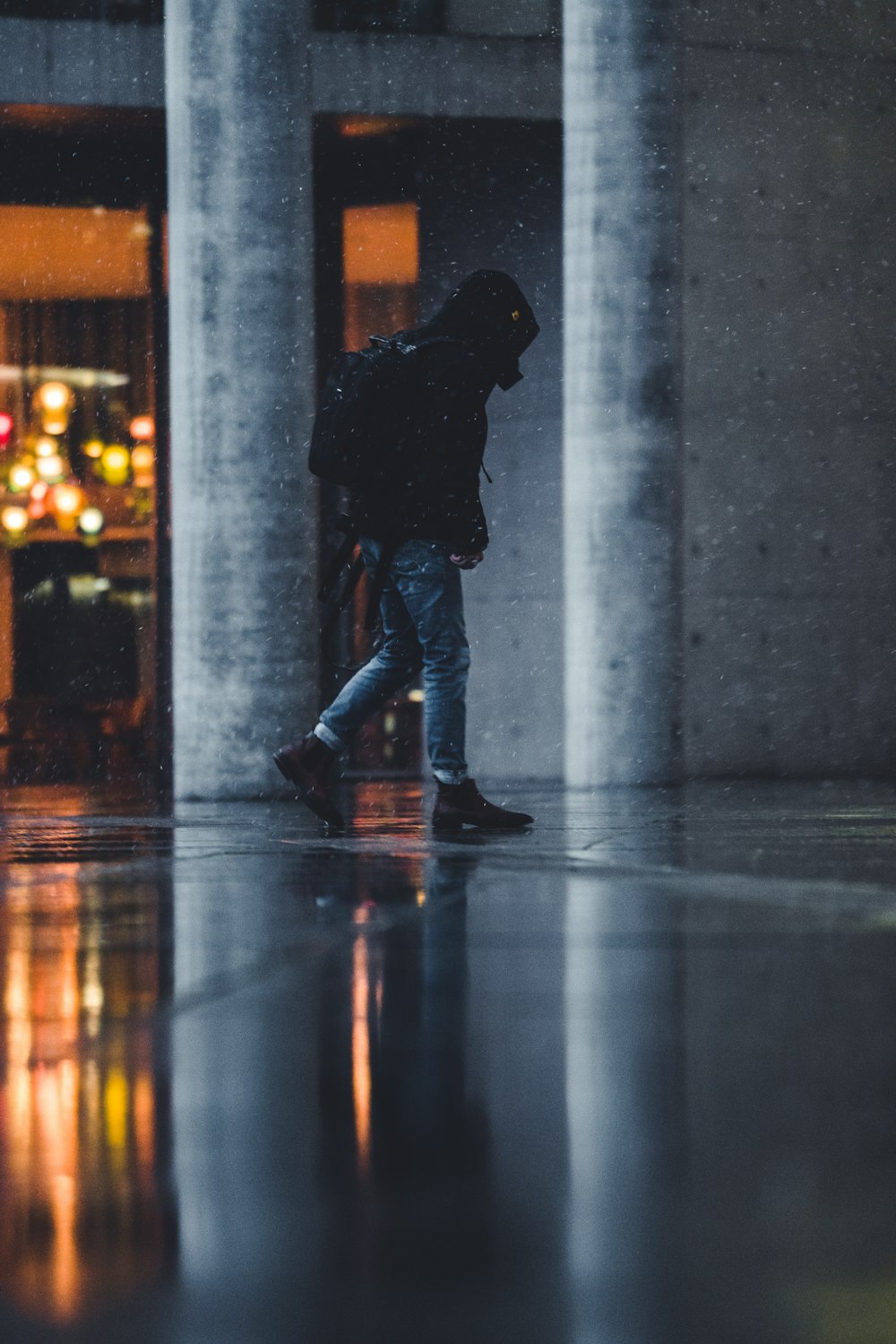 uomo in giacca nera e jeans blu in denim in piedi sul pavimento di cemento grigio