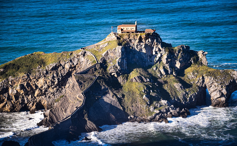 brown house on top of green and gray rock formation beside sea during daytime