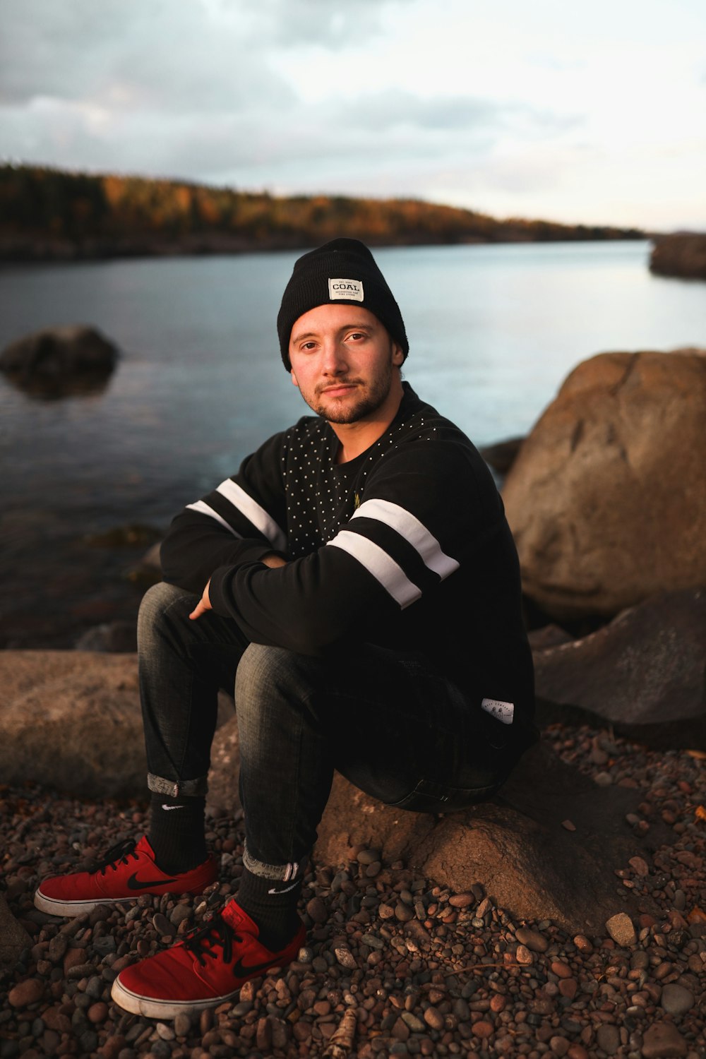 man in black and white striped hoodie and gray pants sitting on rock near body of near near near near