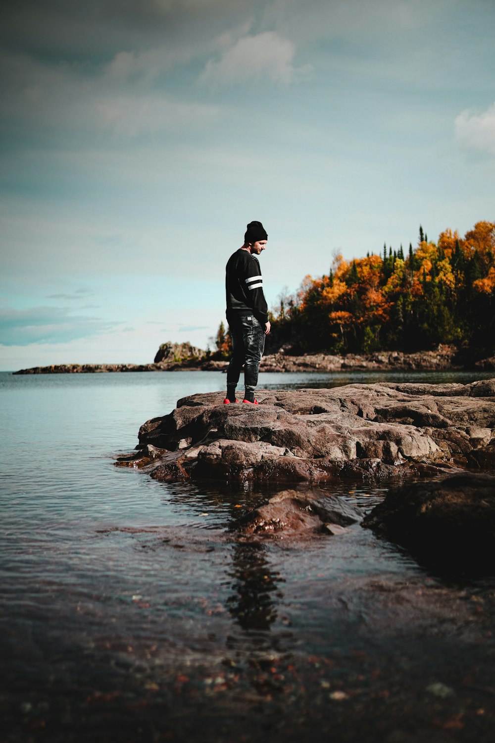 man in black jacket standing on rock near body of water during daytime