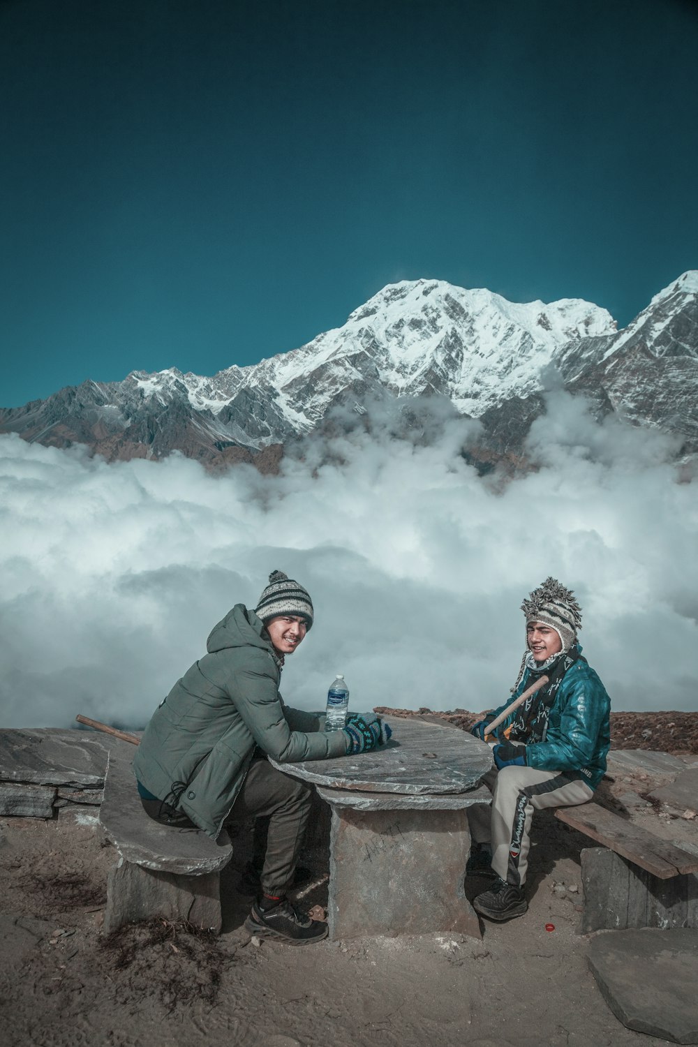 man in green jacket sitting on brown wooden log looking at snow covered mountain during daytime