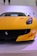 A vibrant yellow sports car is displayed prominently, featuring sleek design elements like a low front profile, aerodynamic curves, and a prominent logo on the grille. The background is minimalistic with parts of letters visible, hinting at a possible exhibition or event space.