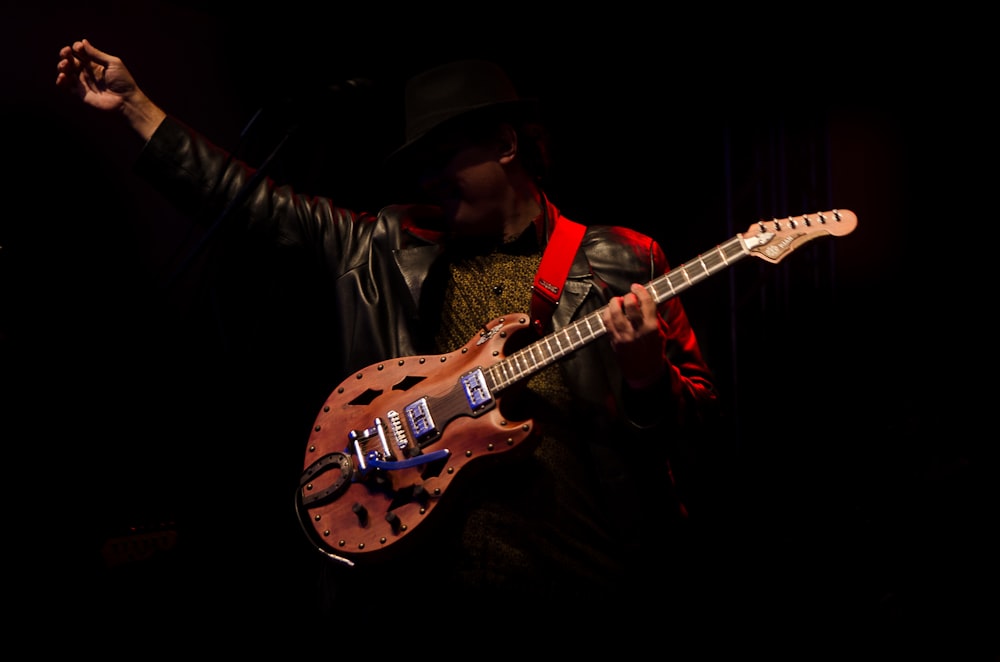 man in black hat playing brown electric guitar